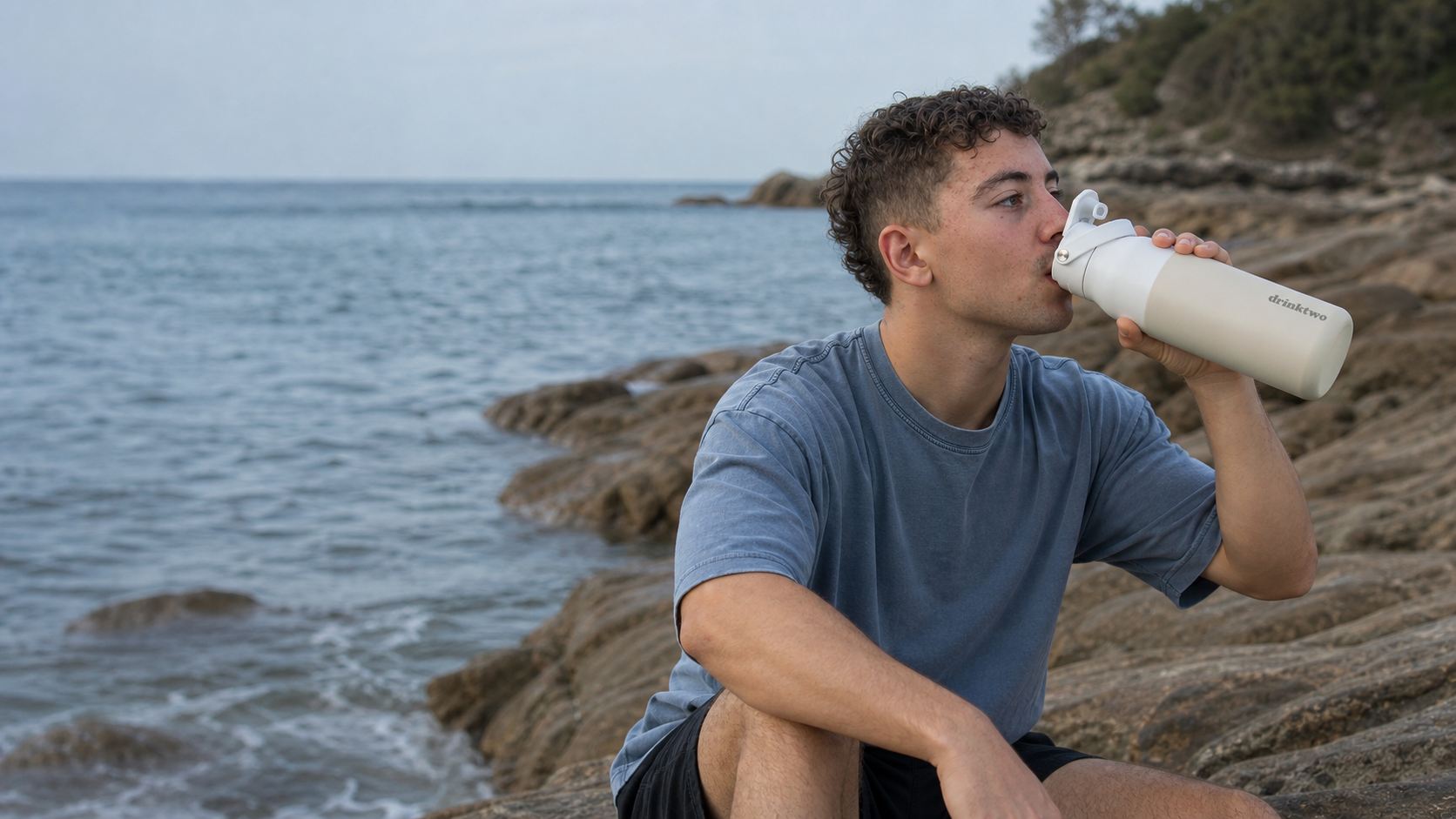 Man drinking from a drinktwo Hydrate bottle by the coast